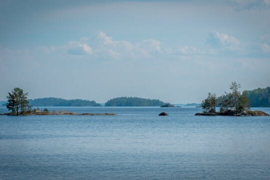 Tranquil view of tree-covered islands on Lake Saimaa reflecting in calm waters under a blue sky.