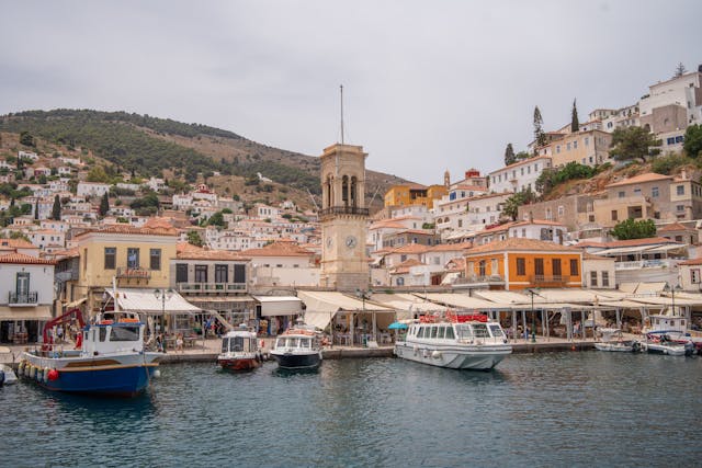 Picturesque harbor in Hydra, Greece featuring moored boats and historic clock tower against hillside houses.